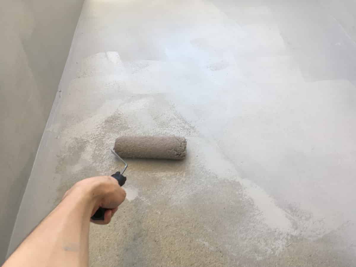 ベランダのセメント床に防水塗料をローラー刷毛で塗る様子