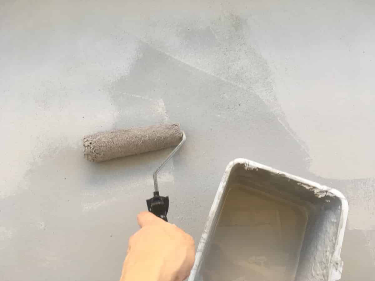 ベランダのセメント床に防水塗料をローラー刷毛で塗る様子（2度塗り）