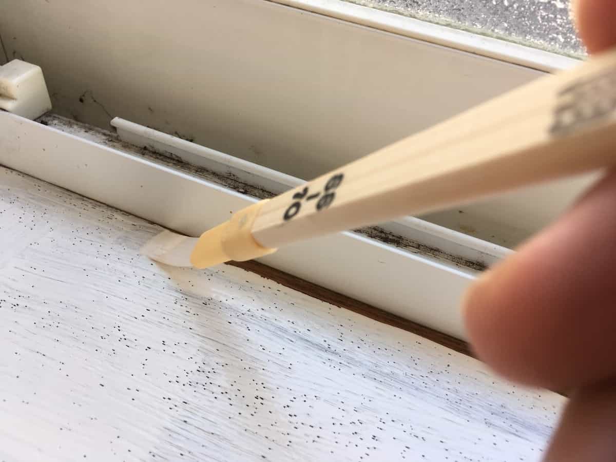 窓枠木部の際を細めの筆で塗る様子